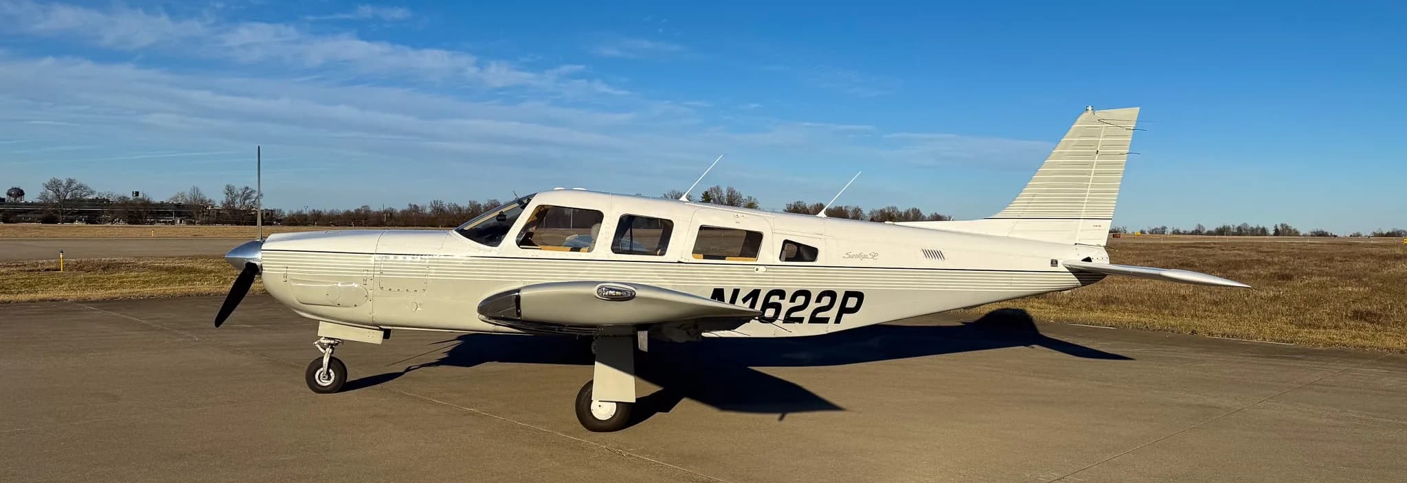 A side view of a white Piper Saratoga SP (N1622P) with grey stripes on an airfield.