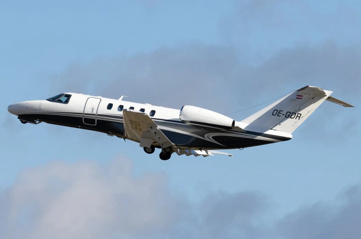A white and dark blue Cessna CitationJet (CJ1) with registration OE-GDR in flight with landing gear extended.