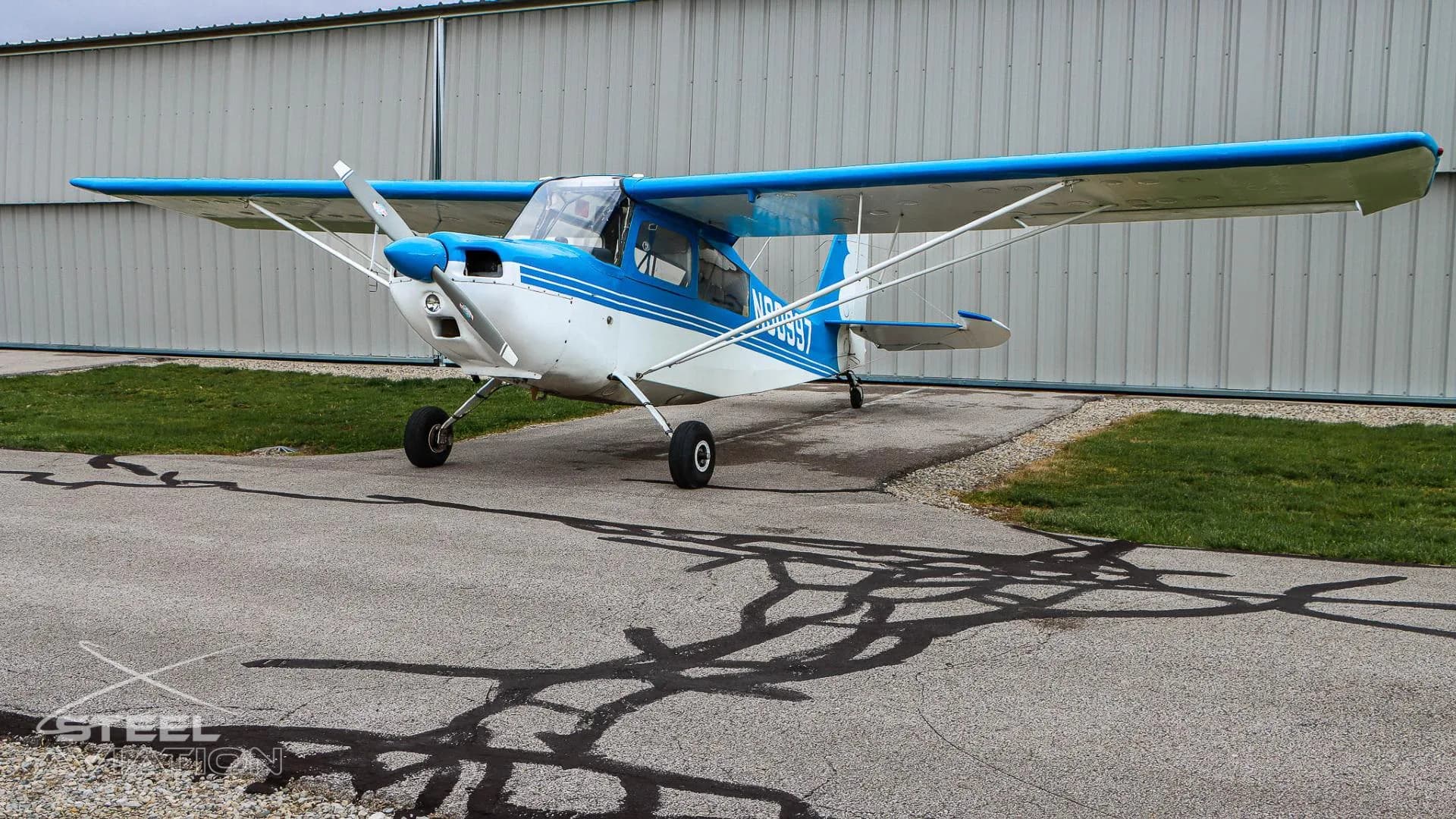 Three-quarter front view of a white and blue Bellanca 7GCBC Citabria aircraft with registration N90997, parked on an asphalt ramp.
