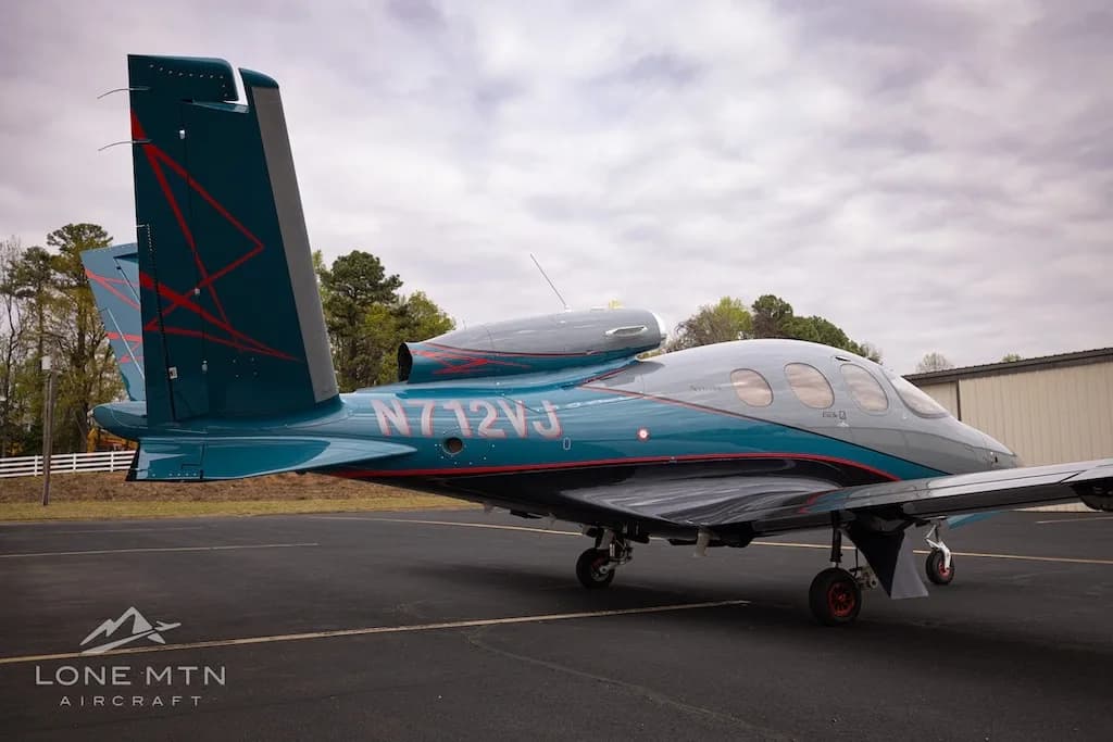 A rear-side view of the Cirrus Vision Jet (N712VJ) showing its V-tail and engine, parked on an airfield.