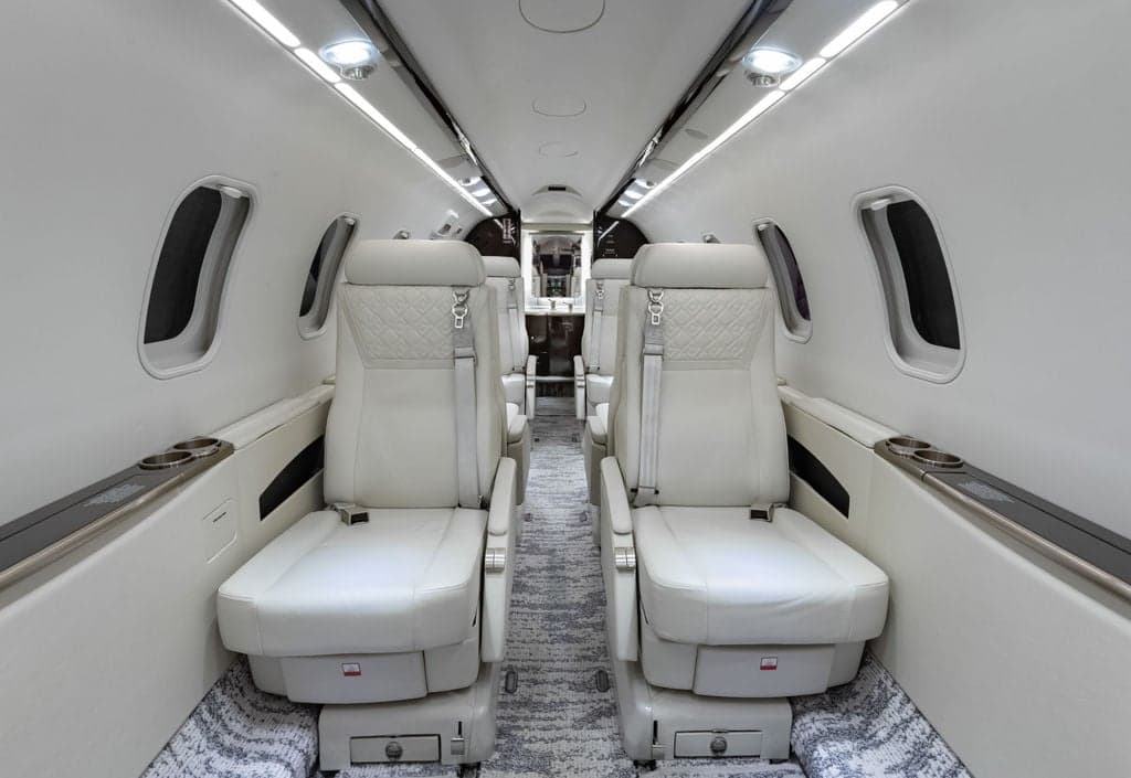 View of the aircraft's interior with white leather seats and carpeted floor.