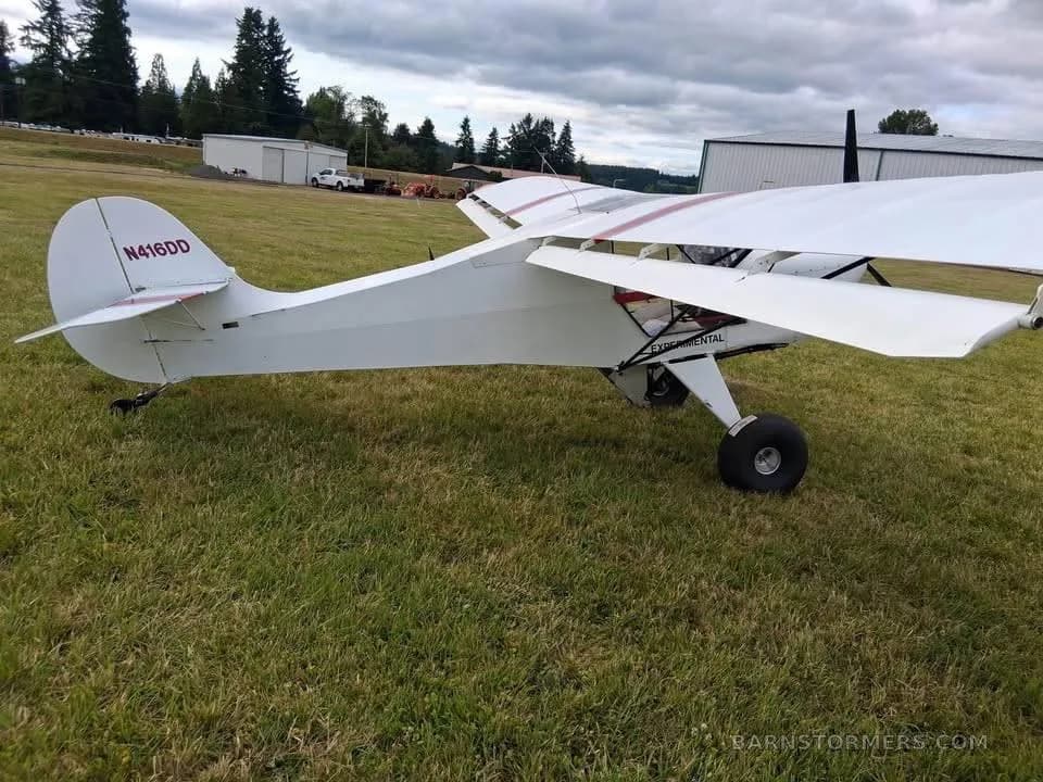 A white experimental aircraft with red stripes on the wing, registration N416DD, viewed from the rear-right on a grassy field.