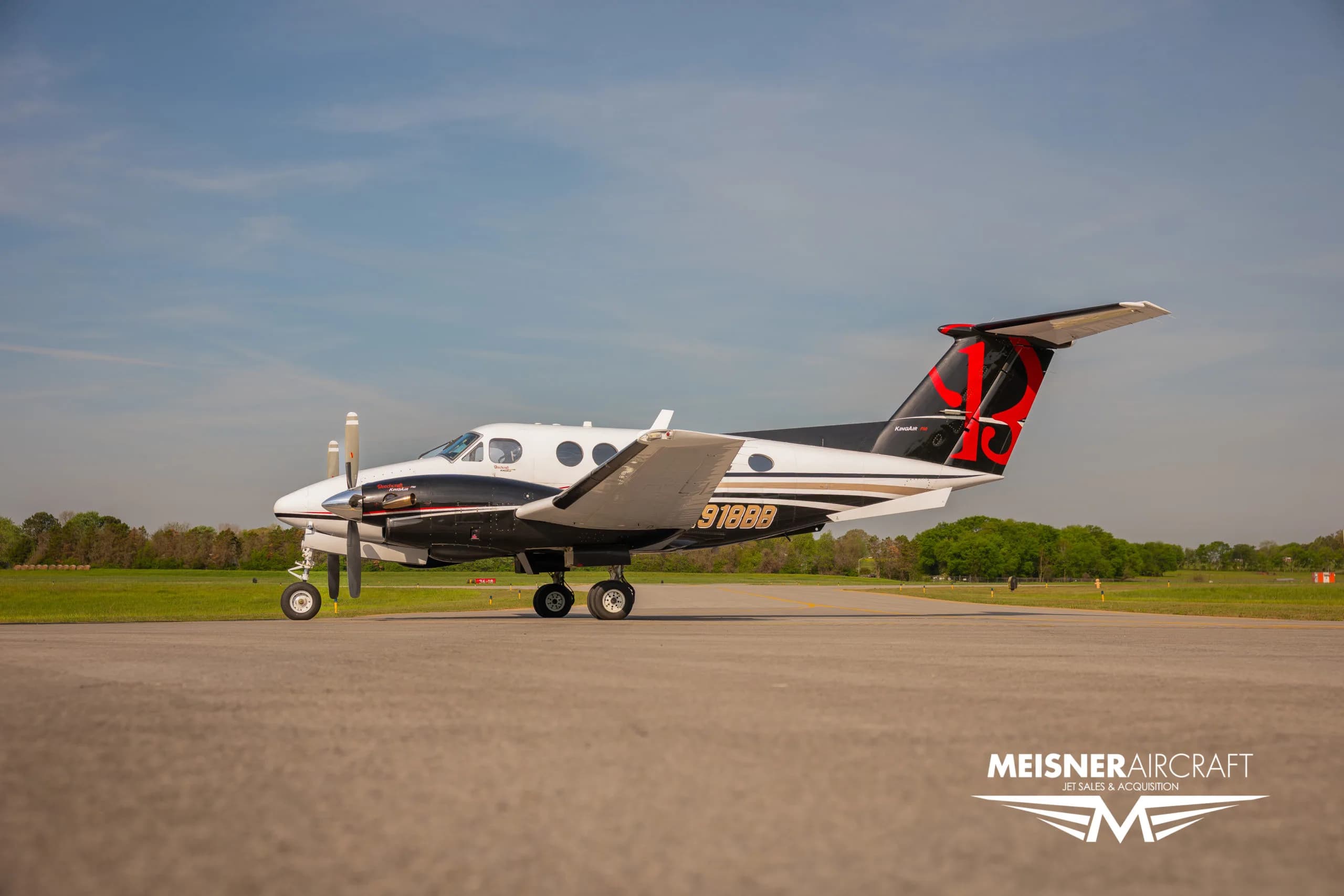 A white and black Beechcraft King Air N918BB with red tail accents parked on an airfield.