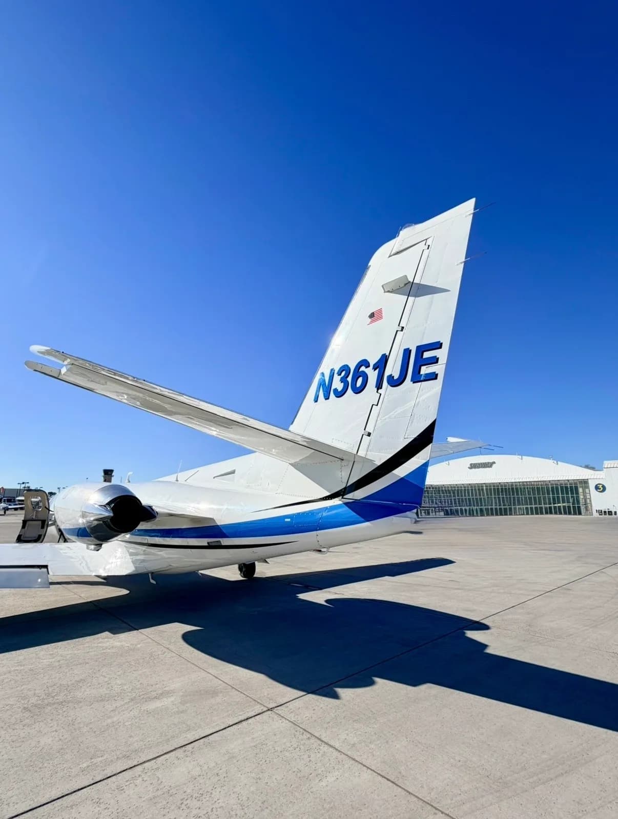 Rear-right view of the tail of a white Cessna CitationJet with blue and black stripes, showing registration N361JE, parked on an airfield.
