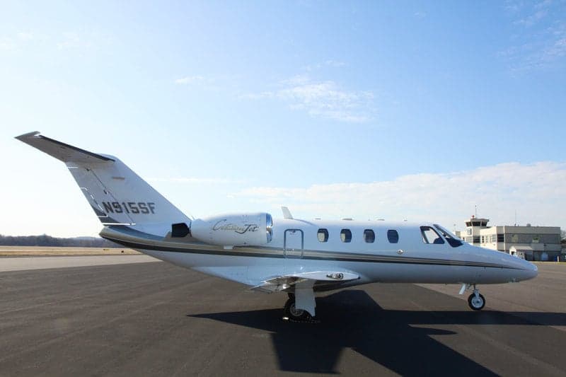A Citation Jet with tail number N915SF sits on the tarmac in front of a control tower.