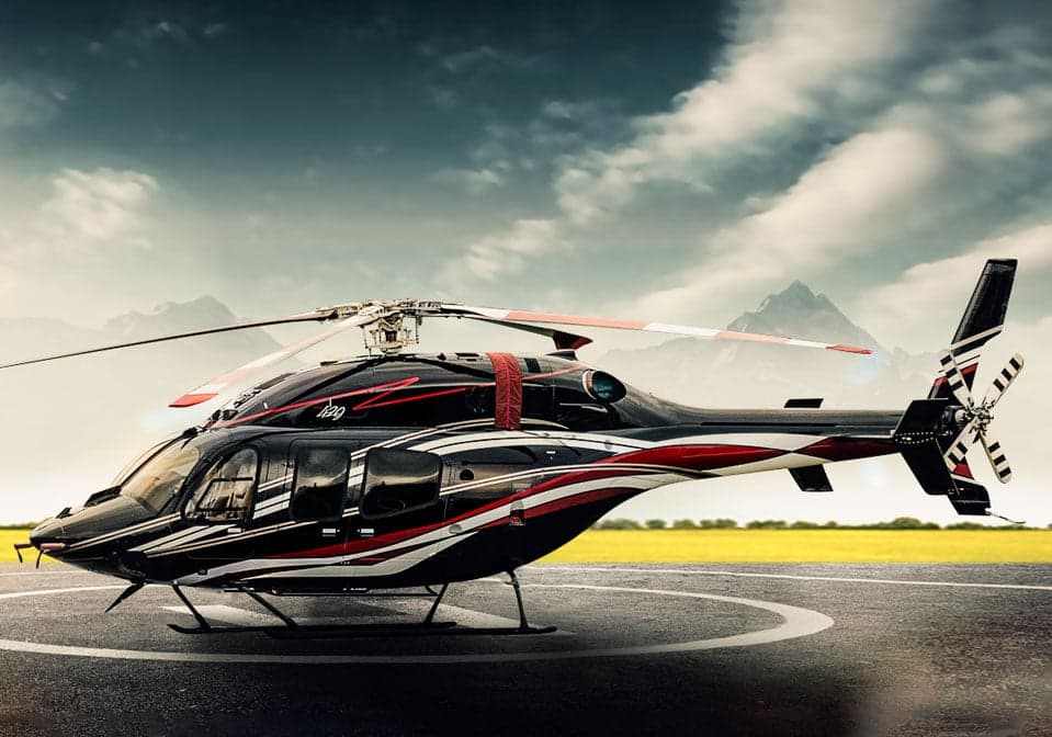 A black and white helicopter with red accents sits on a helipad with mountains in the background.