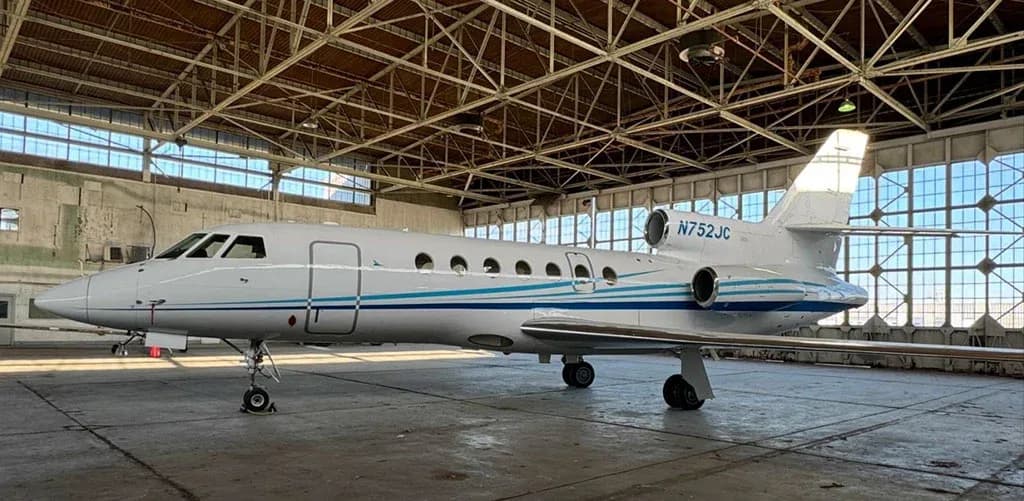 A white business jet with blue and teal stripes, registration N752JC, parked inside a hangar.