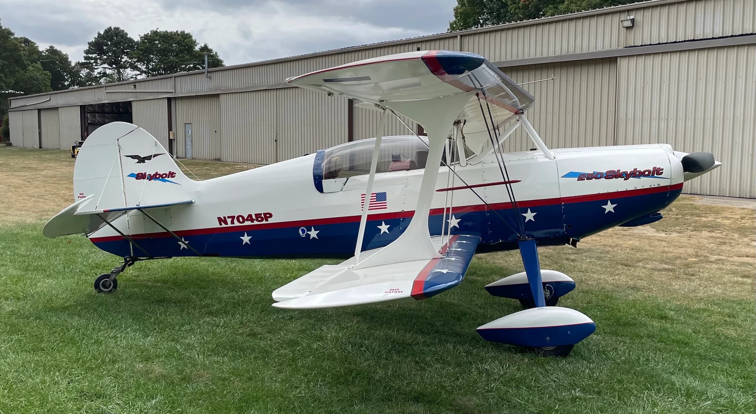 A side view of the white and blue Acro Sport II Skybolt biplane with star decals, parked on grass.