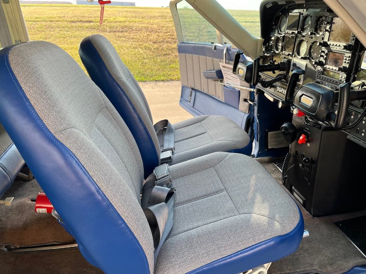 Front seats in the cabin of the Cessna Cardinal RG, upholstered in gray fabric with blue trim, with a view of the cockpit.