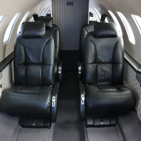 Interior view of a private jet cabin featuring four black leather seats arranged in a club configuration.