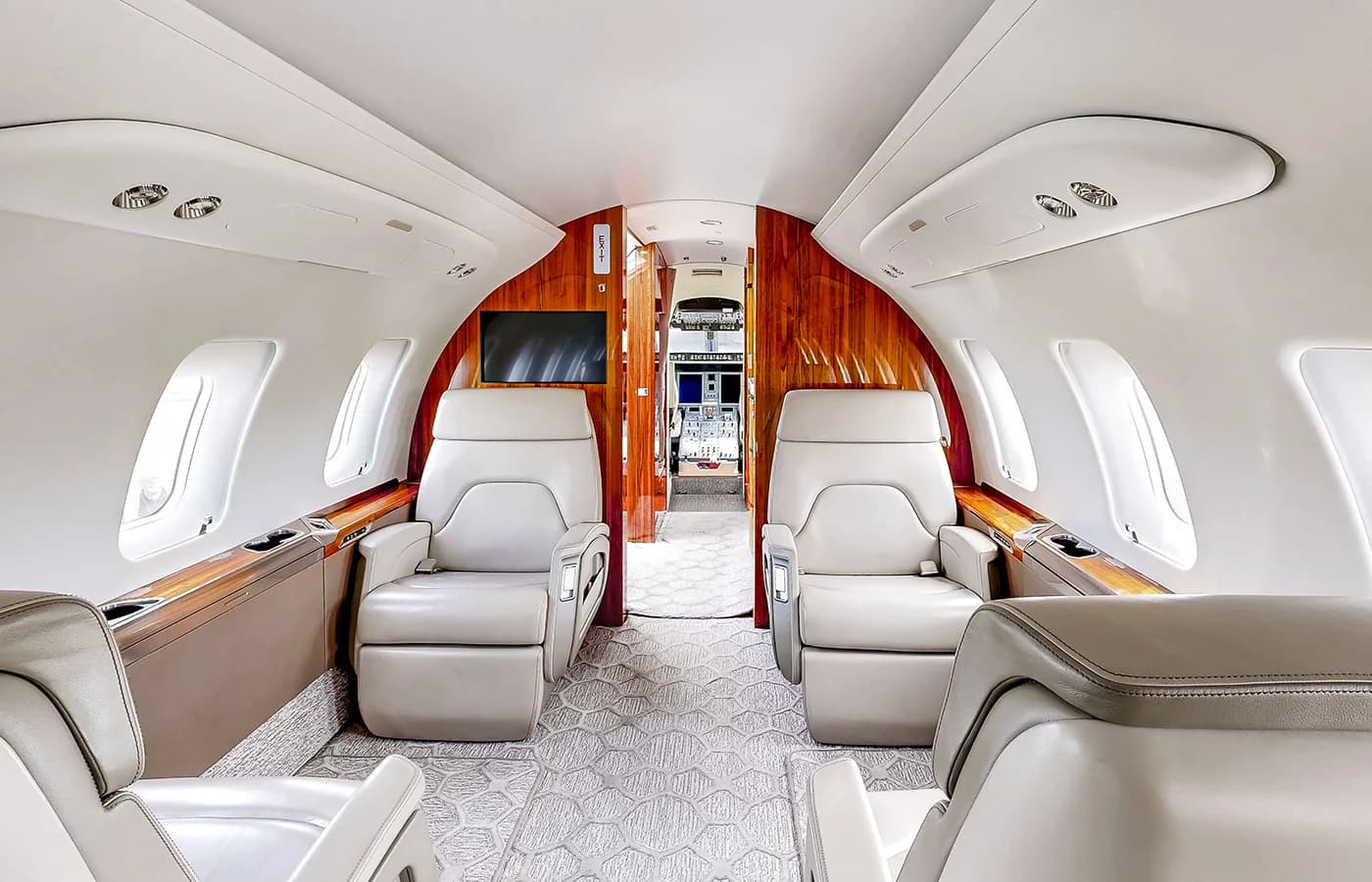 The spacious private jet cabin interior shows rows of beige leather seats and large windows.