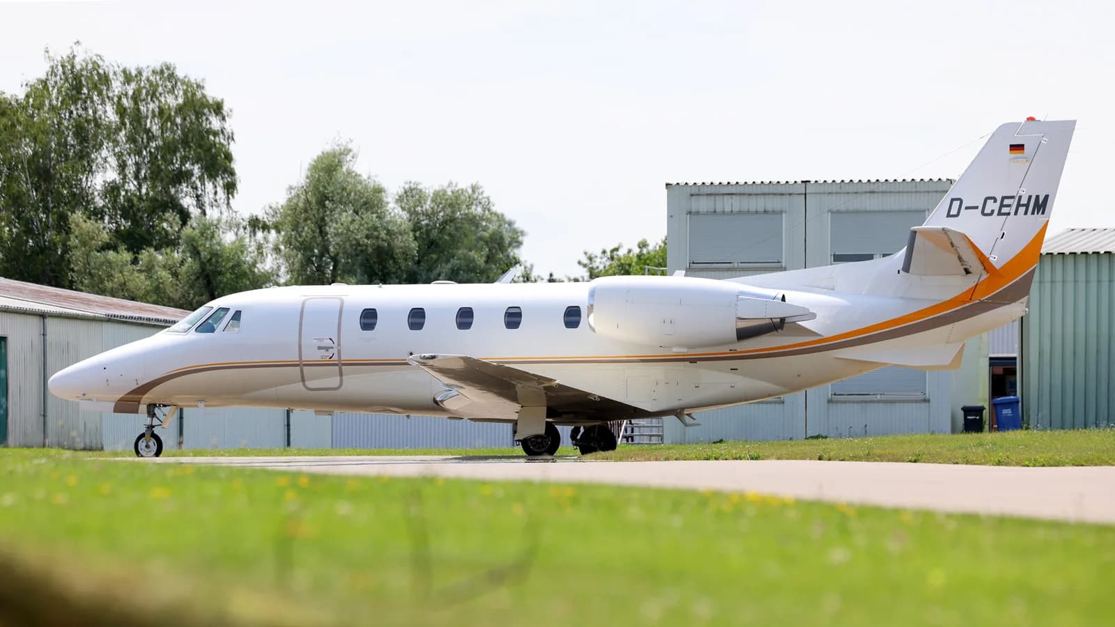 A white Cessna Citation private jet with registration D-CEHM is parked on a tarmac next to hangars.