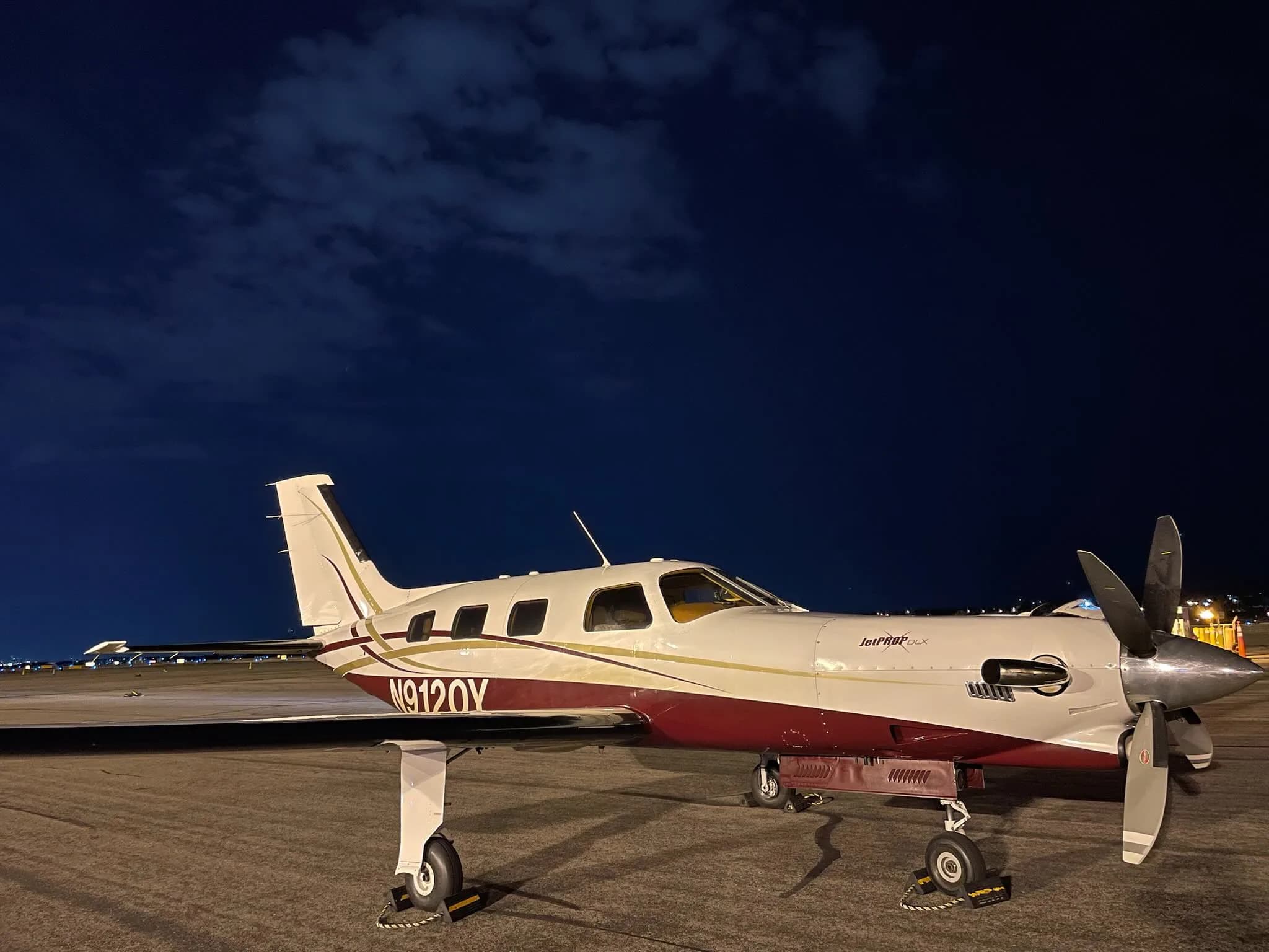 A white and maroon JetPROP aircraft with registration N9120Y parked on the tarmac at night.
