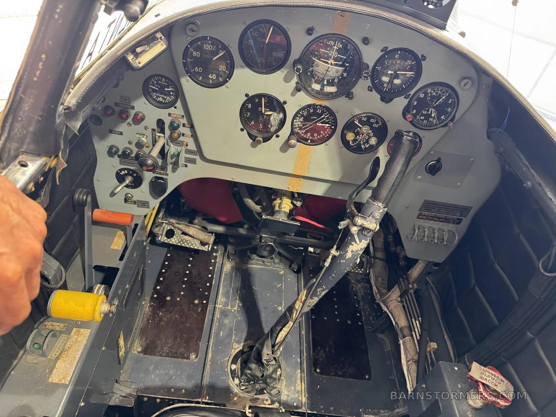 An overhead view of an aircraft cockpit, showing the instrument panel, control stick, and worn floorboards.