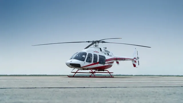 A white and red Bell 505 helicopter with tail number B-70XX is parked on an airfield under a clear sky.