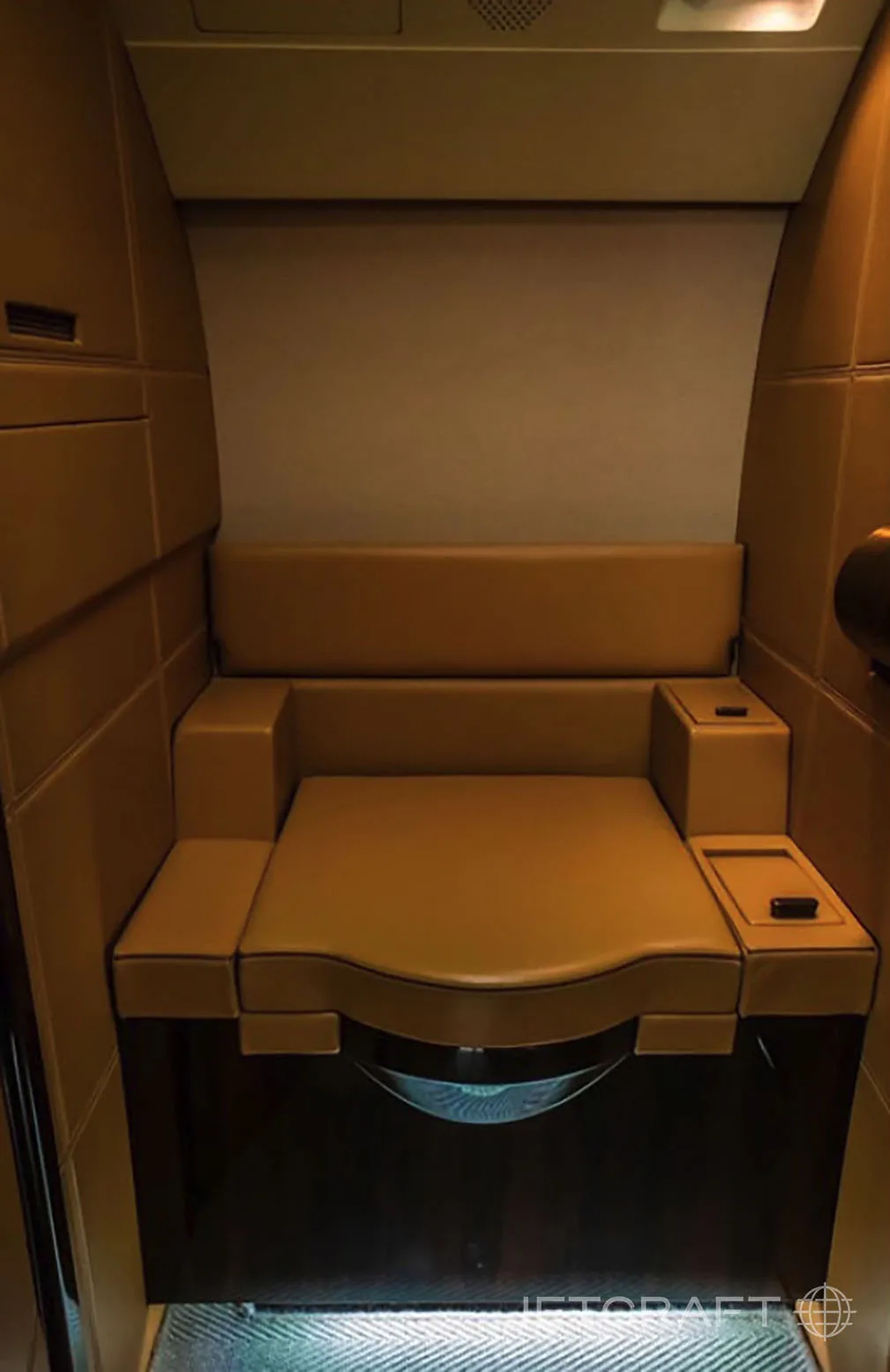A tan leather bench seat with armrests in a private jet interior.