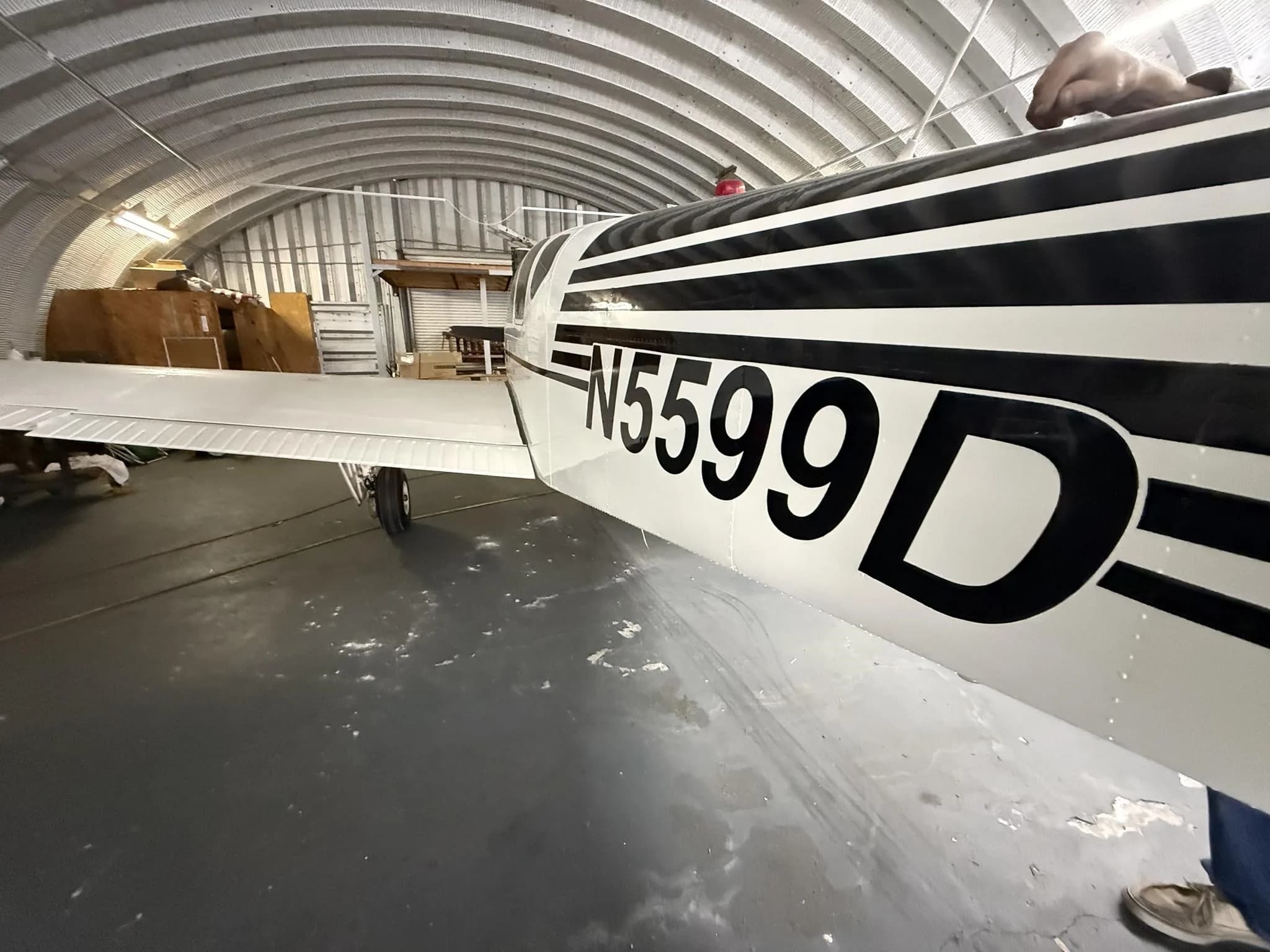 A close-up view of the white fuselage with black stripes and N5599D registration, inside a hangar.
