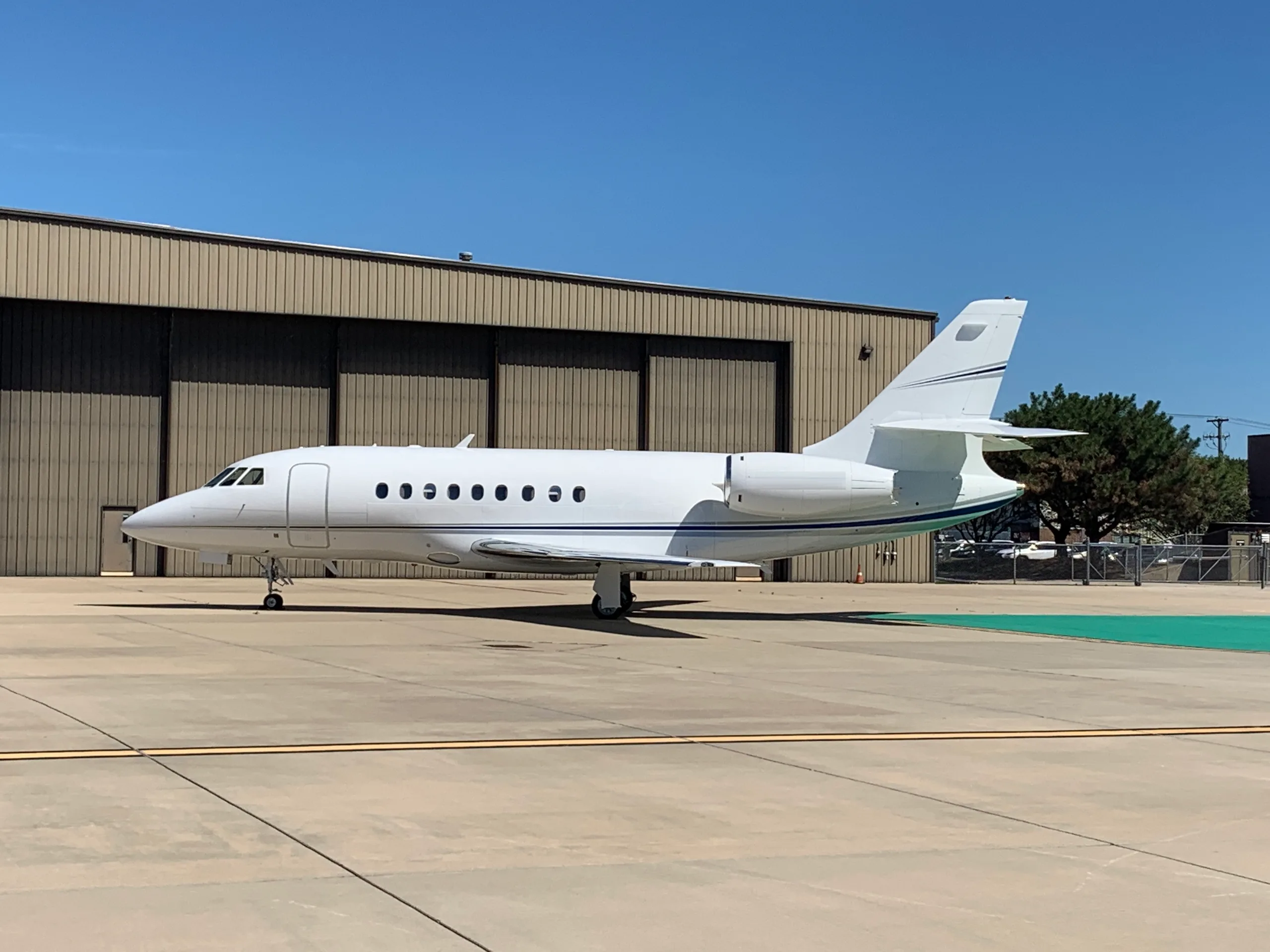 A white Falcon aircraft is parked on the tarmac in front of a hangar.