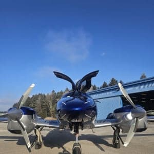 Front view of a blue and silver Diamond DA62 aircraft parked on the tarmac with its gull-wing doors open.