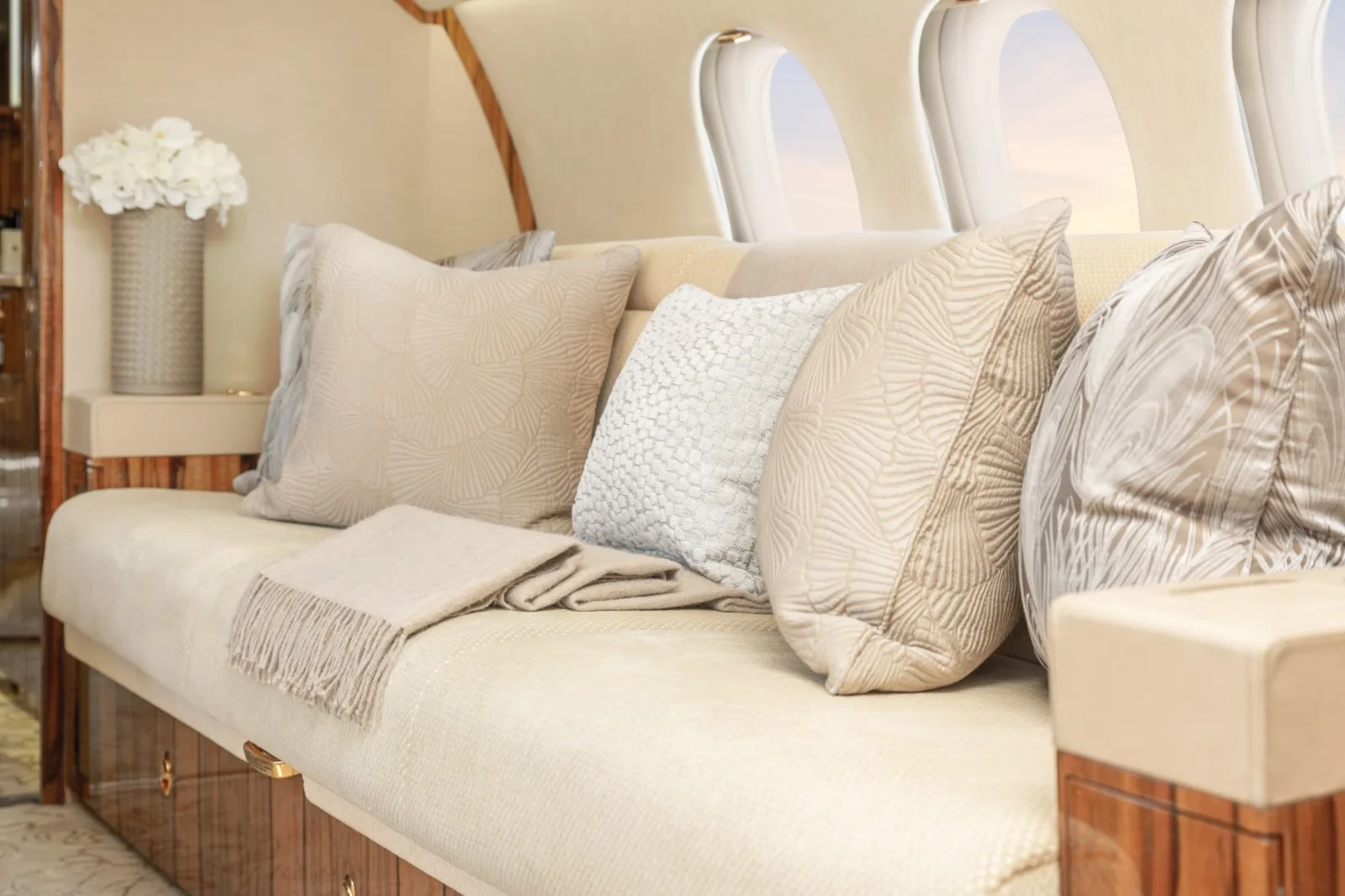 A cream-colored sofa in the aircraft cabin adorned with various textured pillows and a folded blanket.
