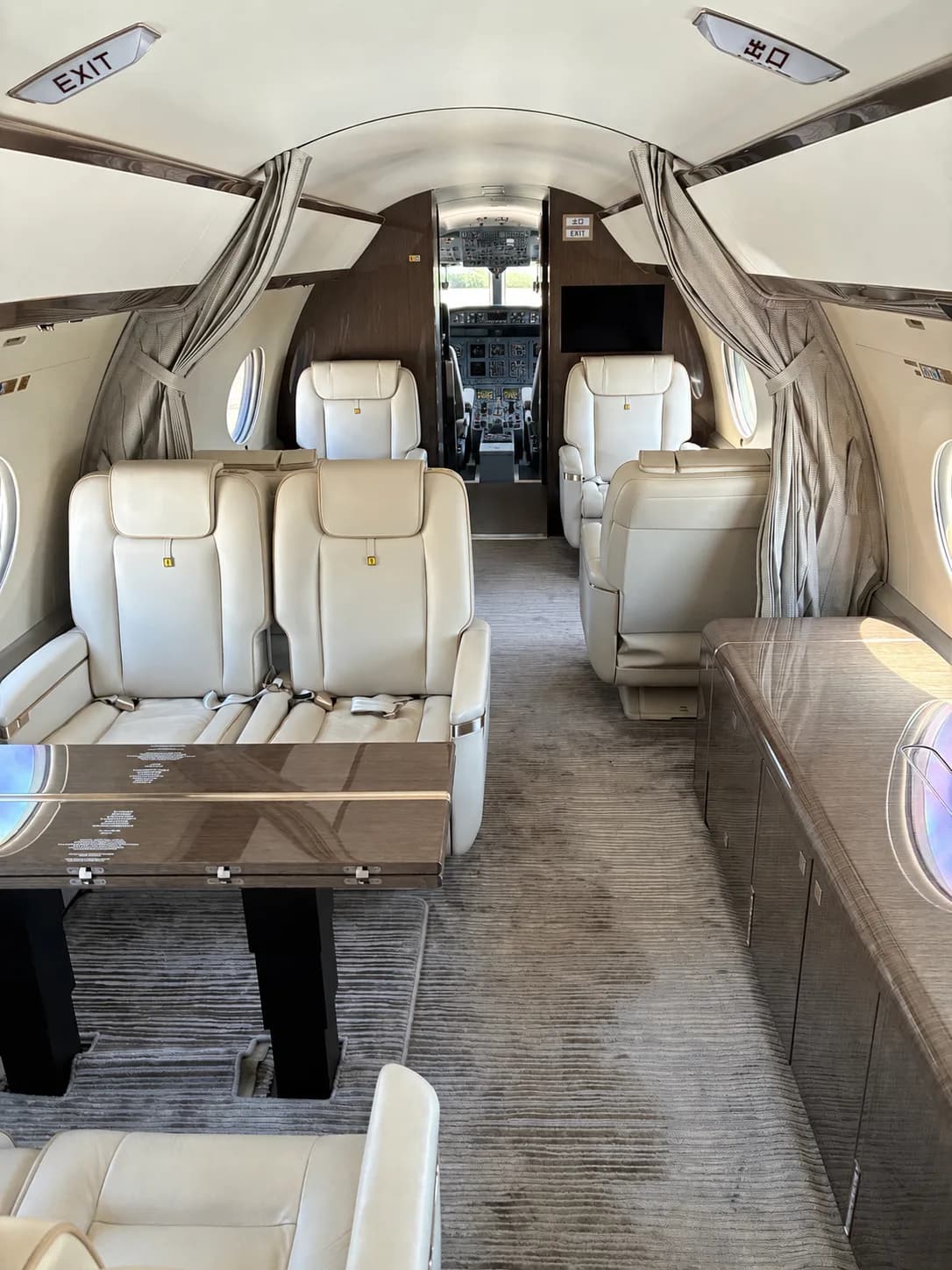 A wide view of the Gulfstream cabin interior, featuring light leather seats, a table, dark wood cabinetry, and a glimpse of the cockpit.