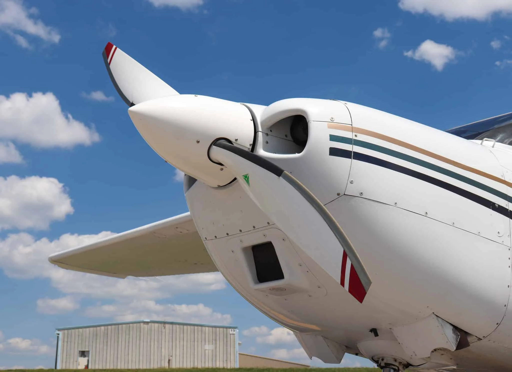 A close-up view of the propeller and nose of a white Cessna 182 Skylane with multi-color stripes.