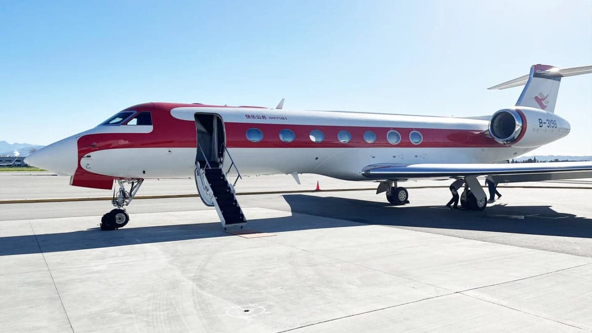 A red and white Gulfstream G650 business jet with its main door open and stairs extended, parked on an airfield.