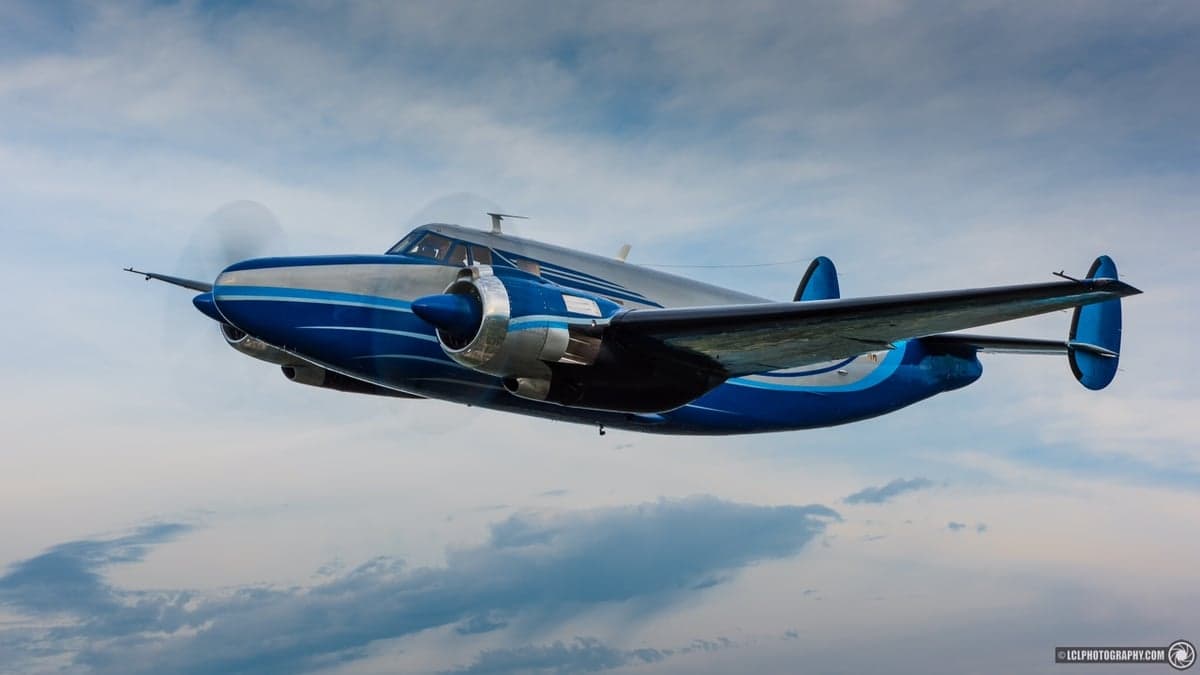 A blue and silver Beechcraft Model 18 flying in the sky.