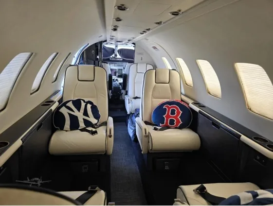 The luxurious interior cabin of a private jet, featuring cream leather seats with New York Yankees and Boston Red Sox pillows.