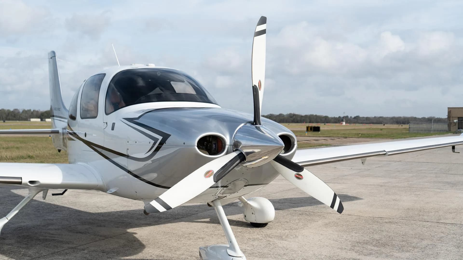 Front 3/4 view of a white Cirrus SR22 aircraft with a three-bladed propeller on an airfield.