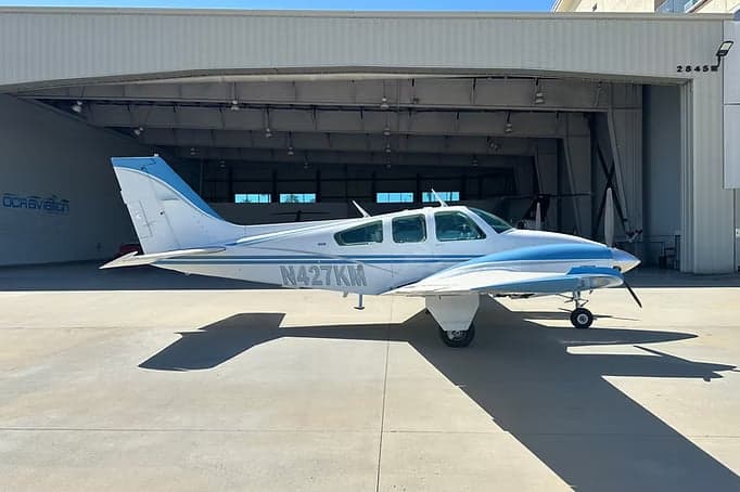A Beechcraft Bonanza with blue and white paint scheme is parked in front of a hangar.