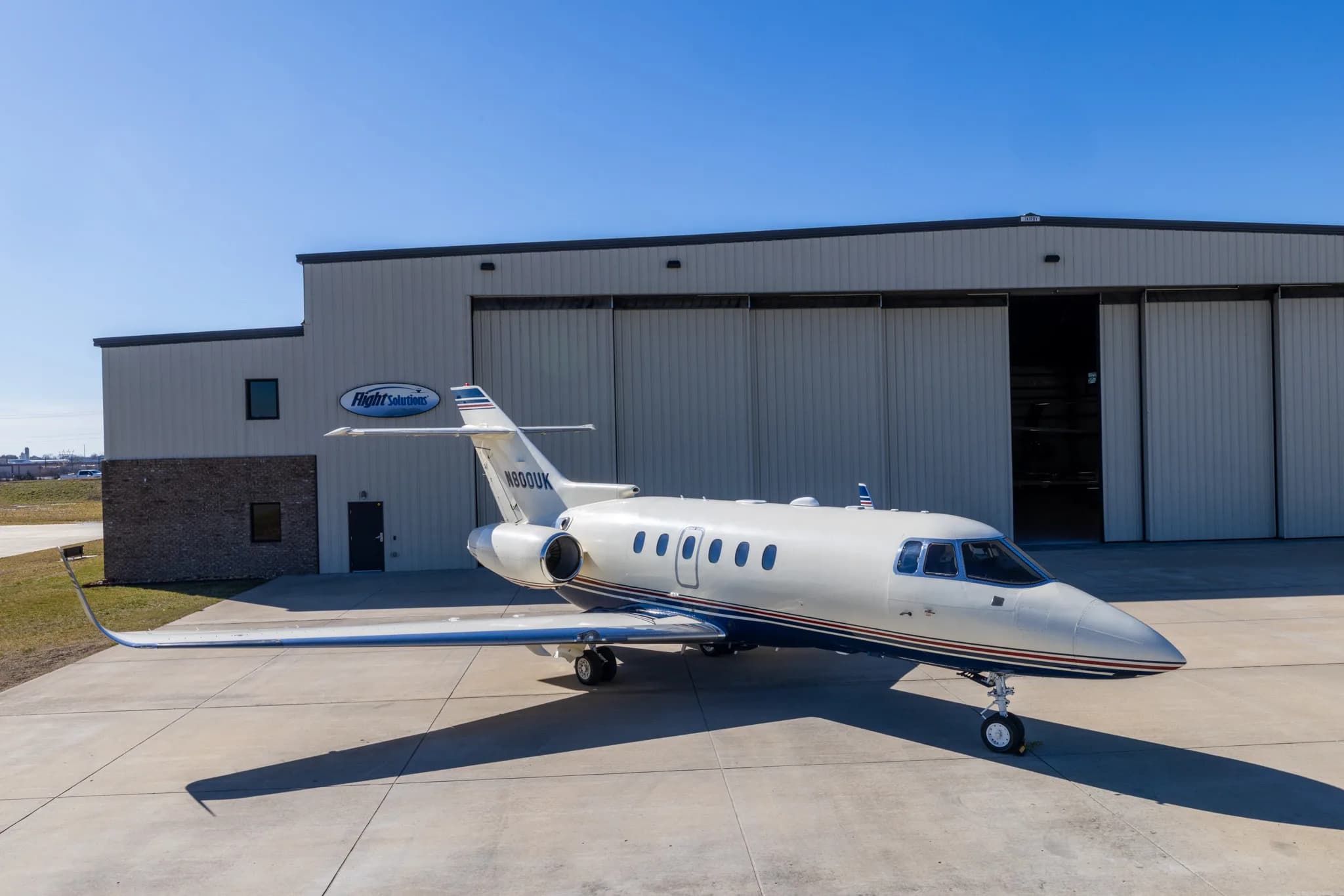 The N800UK business jet is parked on a tarmac outside a large hangar with "Flight Solutions" branding.