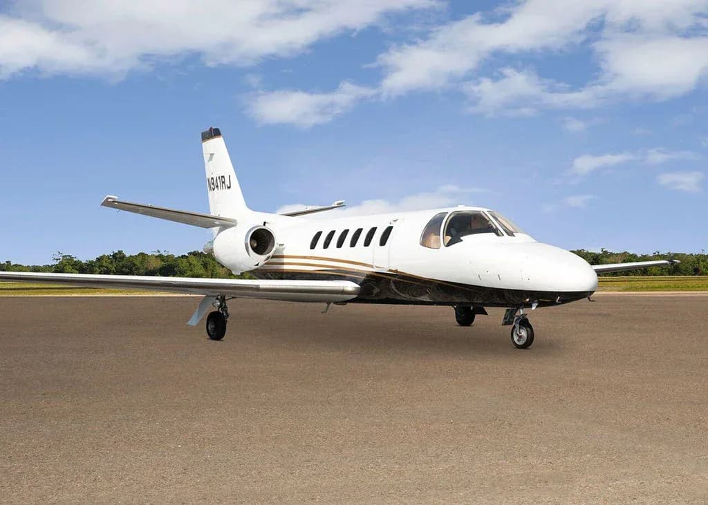 A white and black Cessna Citation business jet N941RJ with gold stripes is parked on a tarmac under a partly cloudy sky, viewed from the front-right.