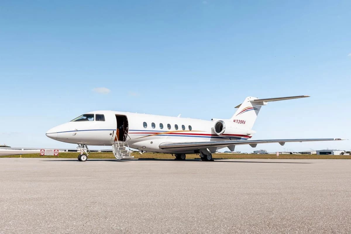 A white Hawker 800XP business jet with red and blue stripes, registration N339RA, parked on the tarmac with its door open and stairs extended.