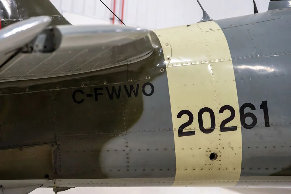 A close-up of the fuselage of a vintage aircraft, showing the registration C-FWWO and number 20261 on a cream band.