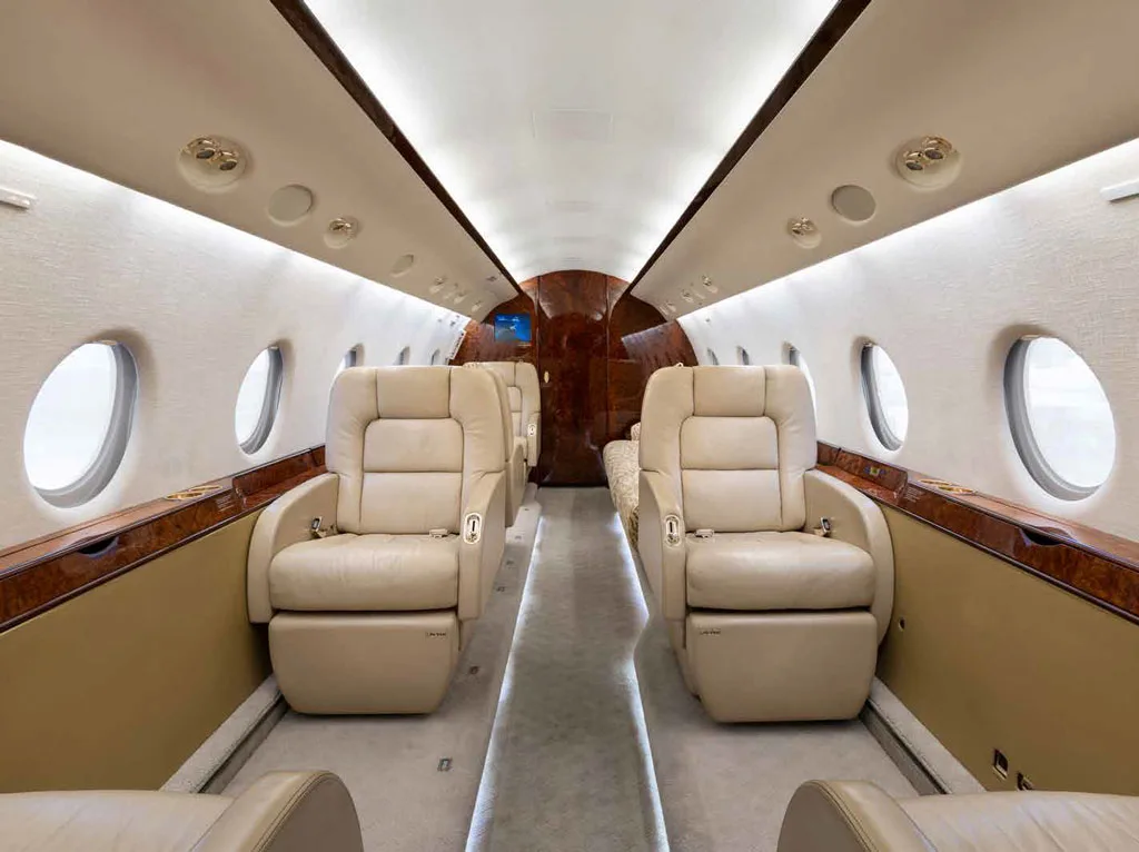 The luxurious cabin interior of a Gulfstream G450 with beige leather seats and polished wood trim.