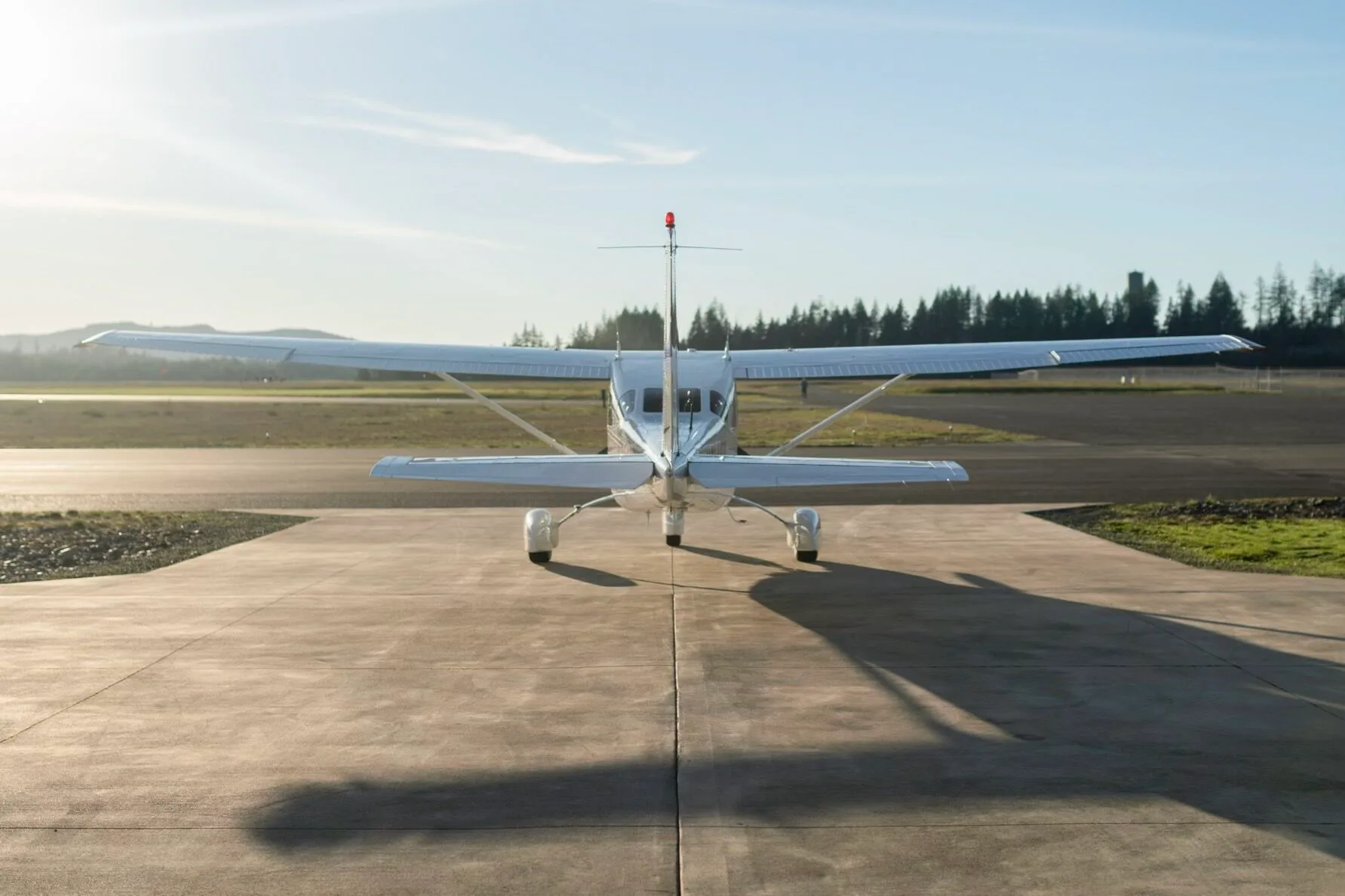 A rear view of a white Cessna aircraft with red tail accents, parked on a tarmac under a bright sky.