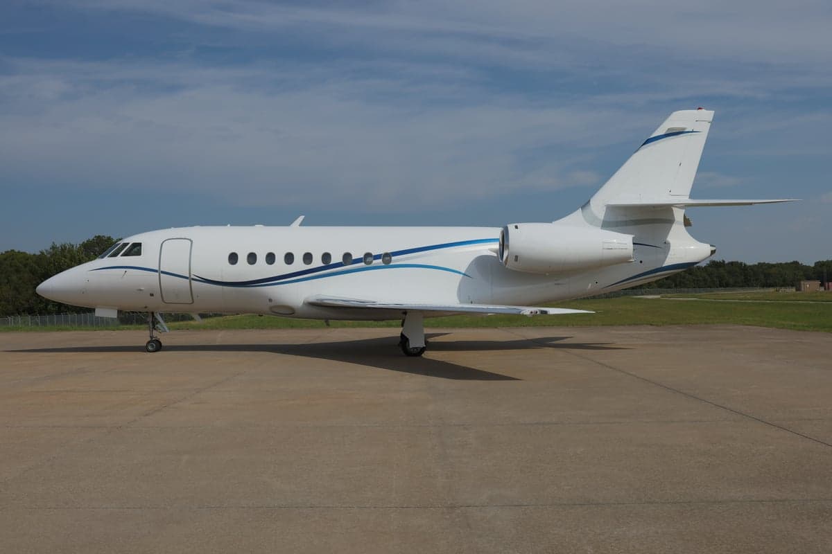 Side view of a white and blue Dassault Falcon jet on the tarmac.