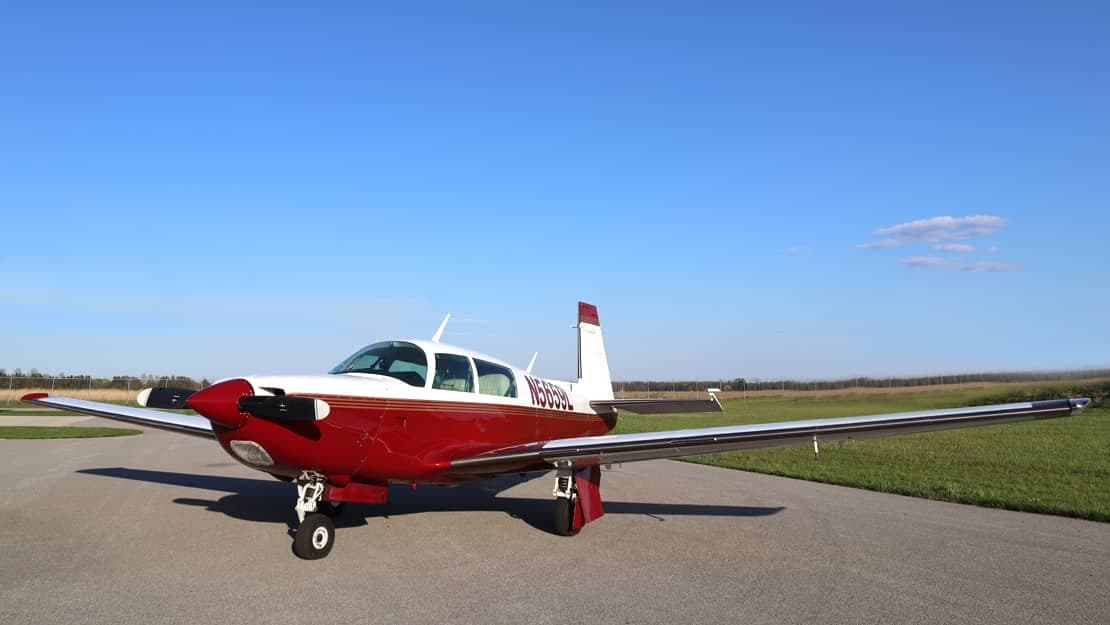 A red and white Beechcraft Bonanza is parked on the tarmac.