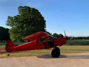 A red Cubcrafters aircraft is parked on a concrete surface.