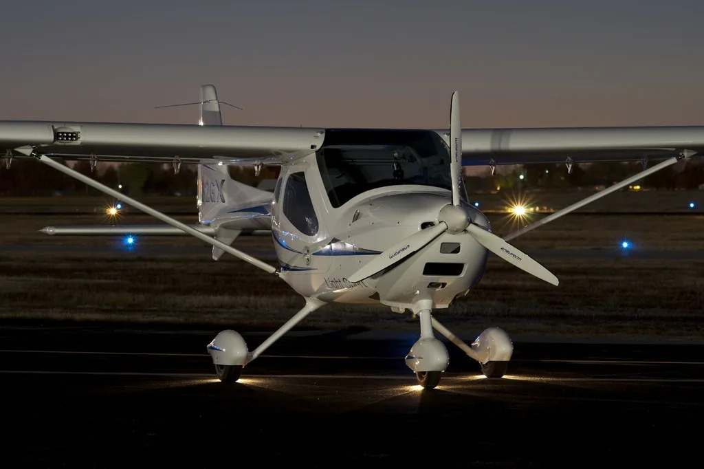 Front view of a white REMOS GX aircraft on the runway at night.