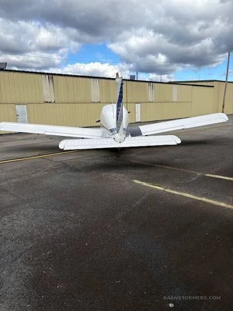 A rear view of a white single-engine propeller aircraft with blue tail stripes parked on an asphalt tarmac.