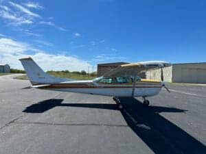 A Cessna 182RG on the tarmac with a white and gold paint scheme, viewed from the side.