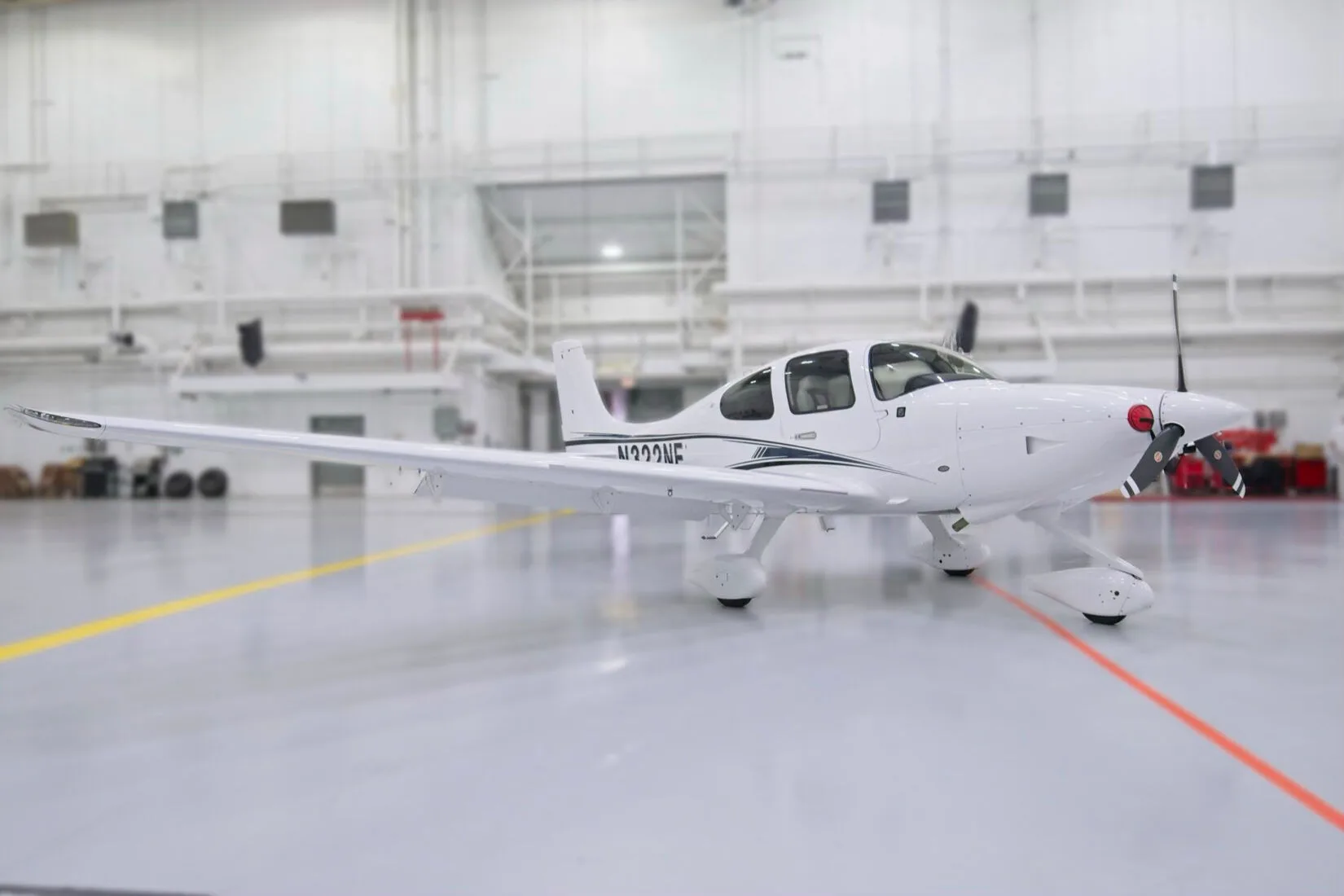 A front three-quarter view of a white Cirrus SR22 aircraft with black and blue stripes, N322NE, in a hangar.