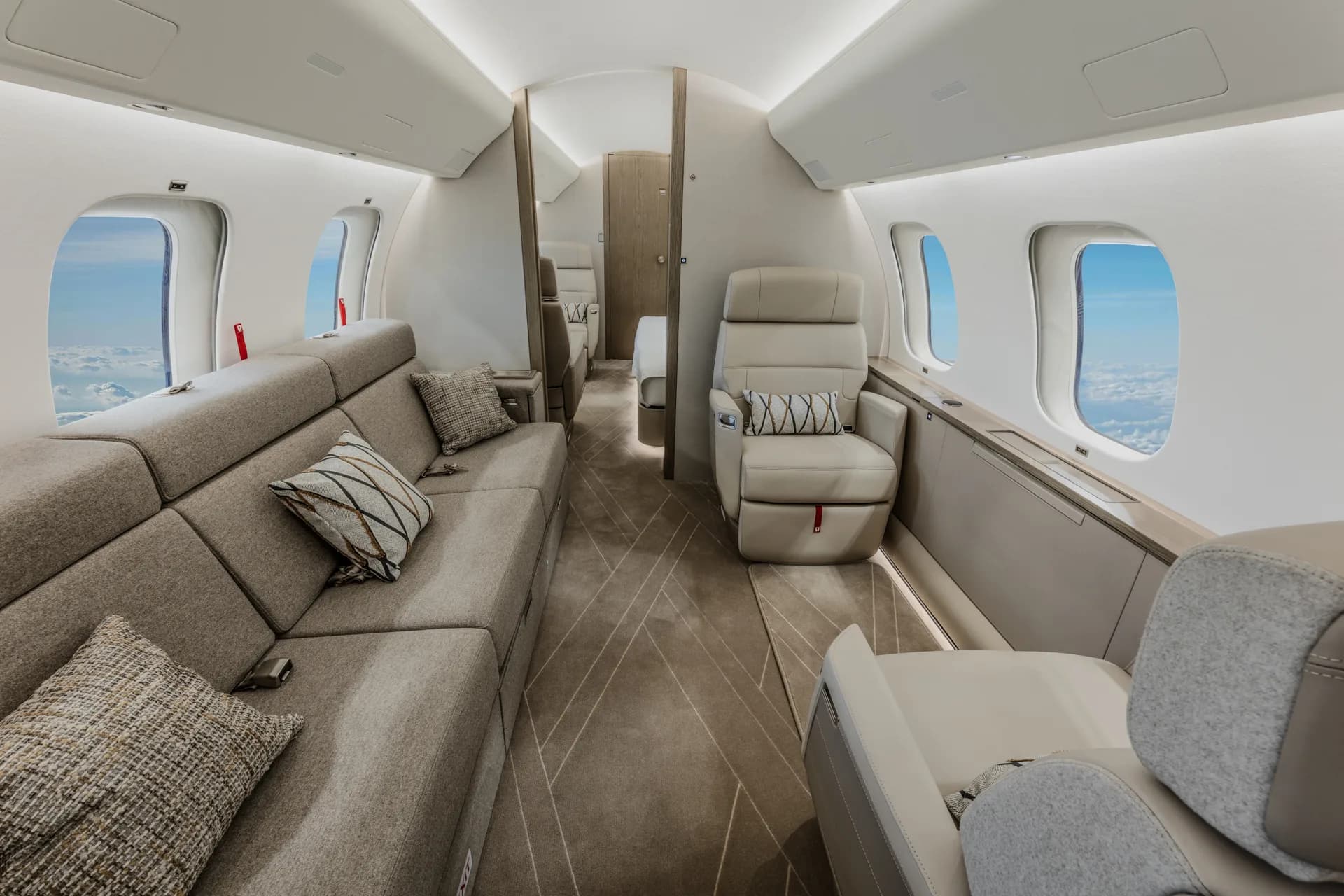 A private jet cabin with a long grey sofa on the left and a single cream leather seat on the right.