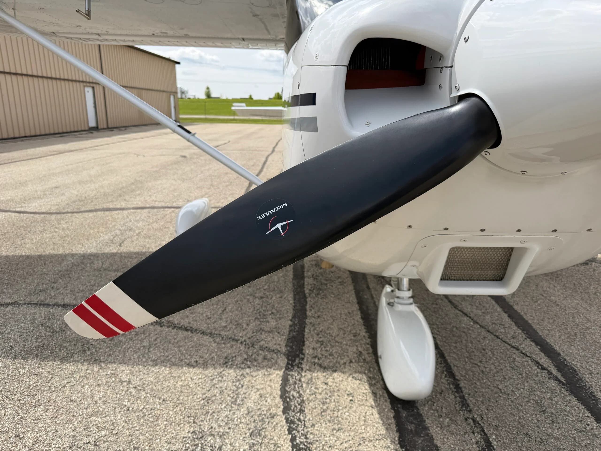 A close-up of the black McCauley propeller with red and white tips on the front of the aircraft.