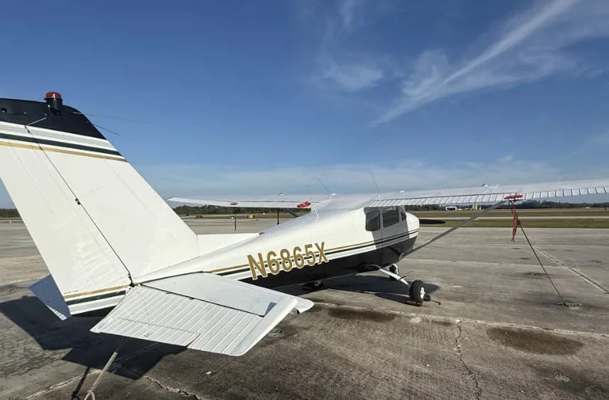 A rear-quarter view of a white and black Cessna 172 with registration N6865X on the fuselage, parked on an airfield.