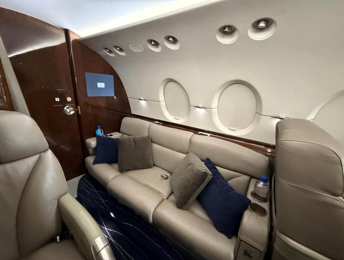 Aircraft interior with leather couch and blue pillows.
