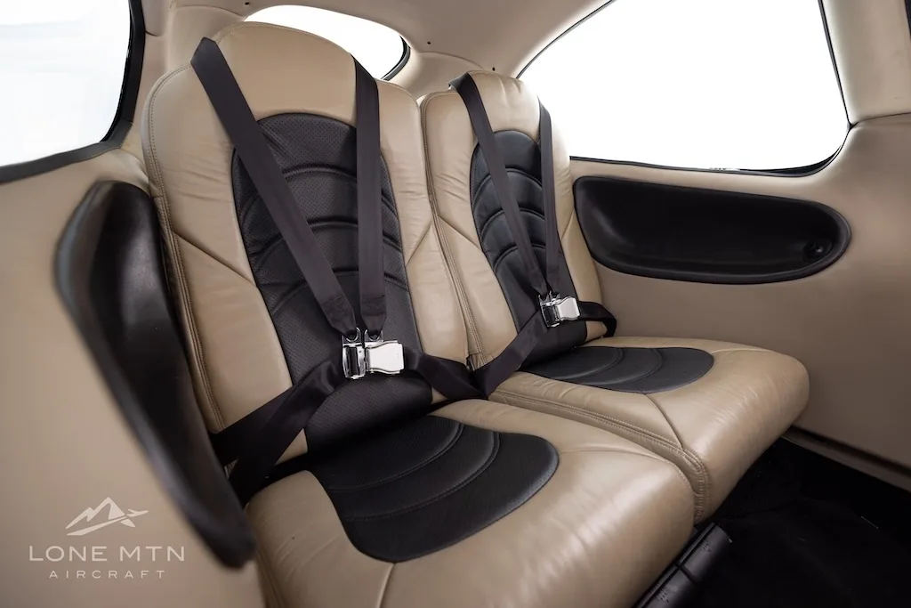 Interior view of two tan and black aircraft seats with harnesses in the cabin.