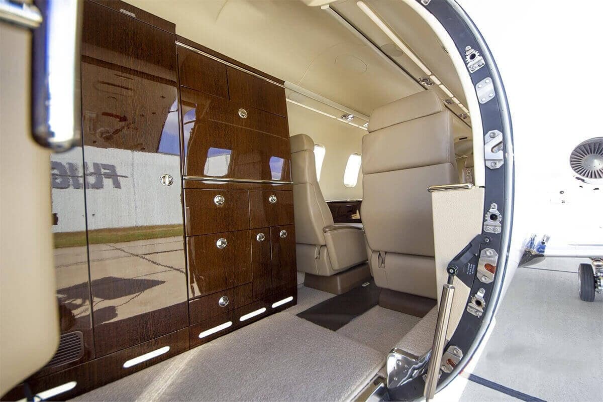 The aircraft interior features a wood cabinet and leather seats.